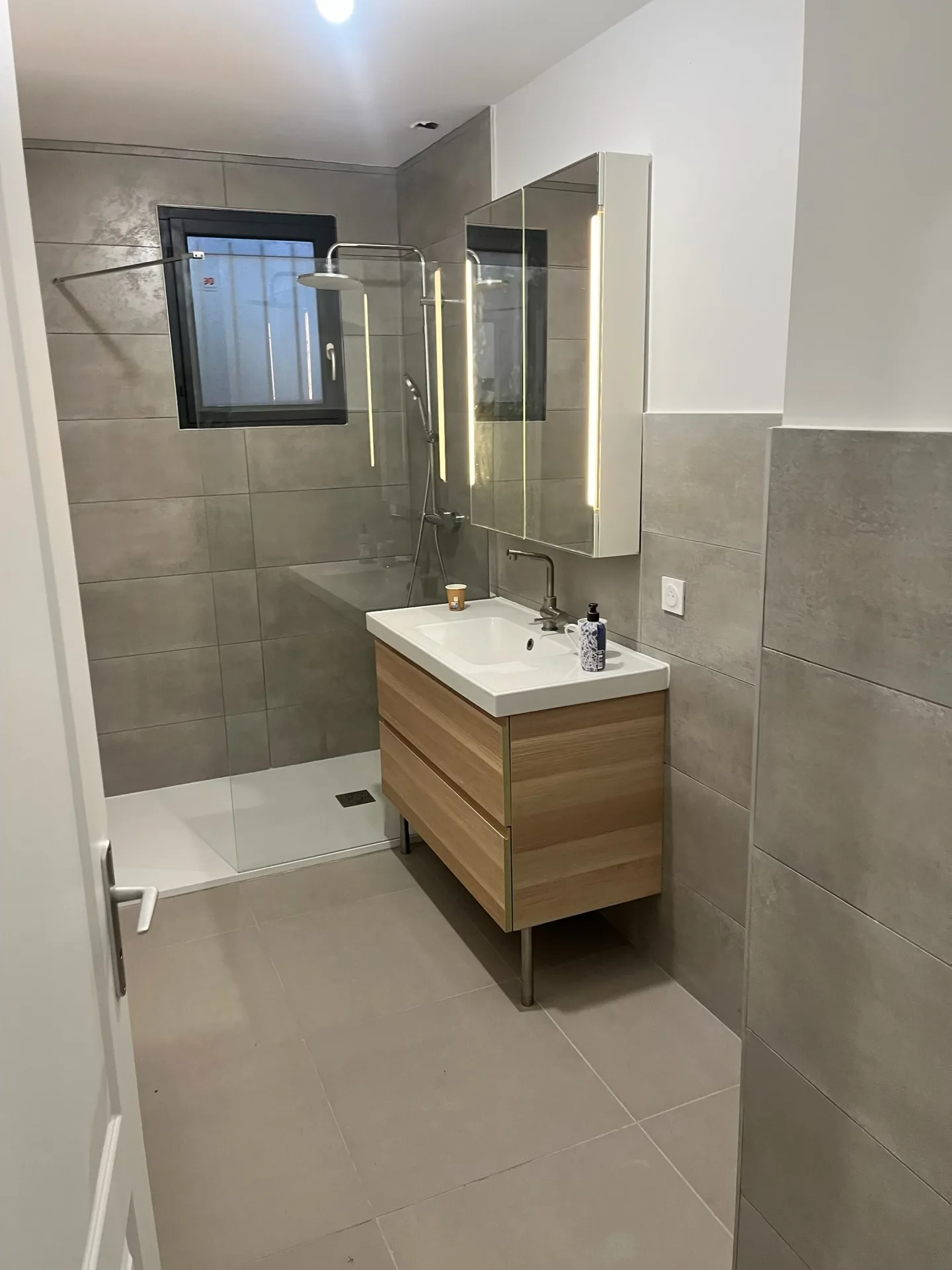 Salle de bain moderne après rénovation — carrelage gris, meuble vasque bois, douche vitrée